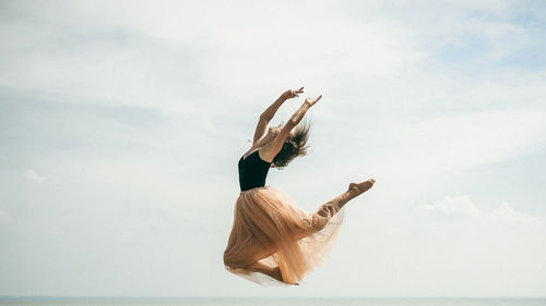 Side view of young woman jumping by sea against sky