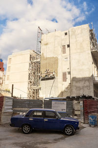 Cars on road by buildings against sky in city