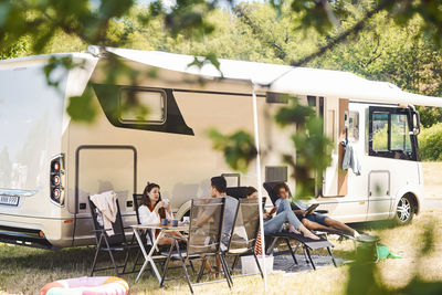 Family relaxing on chairs outside camper van at campsite during summer vacation