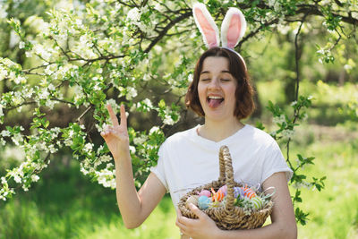 Funny teen girl with eggs basket and bunny ears on easter egg hunt in sunny spring garden