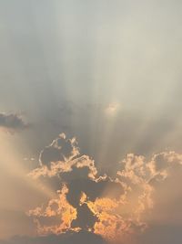 Low angle view of sunlight streaming through clouds