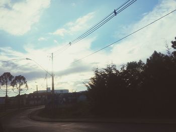 Silhouette trees by road against sky