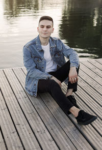 Portrait of young man sitting on pier over lake