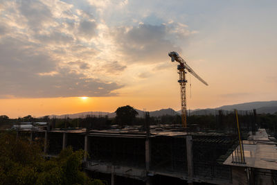 Cranes at construction site against sky during sunset