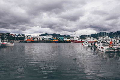 Boats in river against cloudy sky