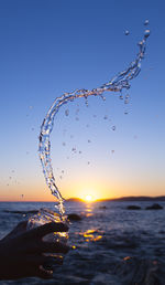 Cropped hand splashing water in jar by sea during sunset