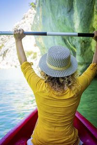 Rear view of woman with hat sitting on riverbank