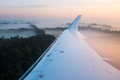 Aircraft wing over landscape against sky during sunset