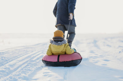 Father pulling son siting on inflatable tube in winter