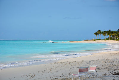 Two empty chairs on idyllic beach against blue sky