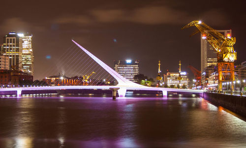 Illuminated bridge over river in city at night