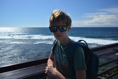 Portrait of young man wearing sunglasses standing against sea