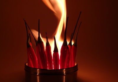 Close-up of lit tea candle with red chili pepper against red background