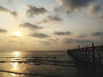 Wooden jetty on beach against cloudy sky