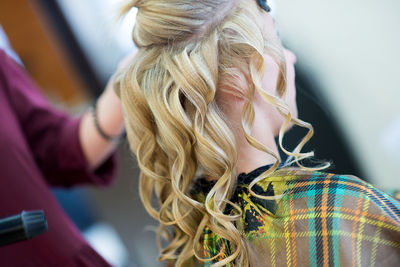 Cropped image of female hairdresser using equipment on blond bride at salon