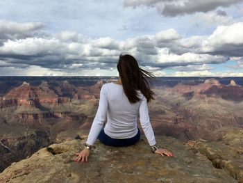 Rear view of woman sitting on rock against sky