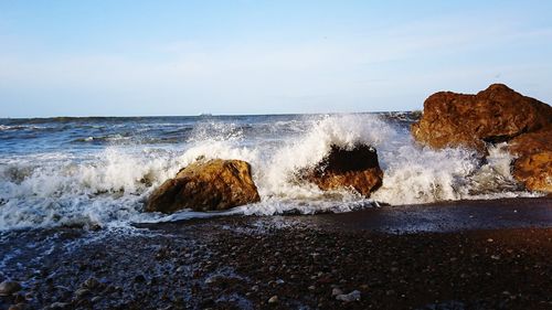 Waves splashing on rocks at shore against sky