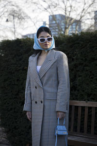 Portrait of young woman wearing sunglasses standing against trees