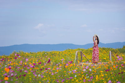 Woman standing by flowering plants on field against sky