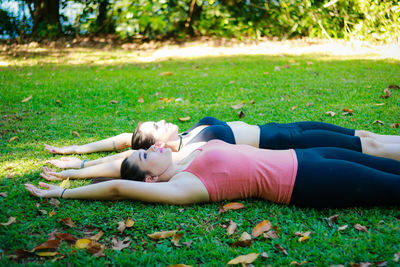 Side view of young female friends lying down on grassy field