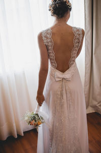 Rear view of bride holding flower bouquet while standing at home