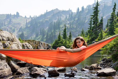 Woman is peeking out of a hammock at the alpine lake on local vacation