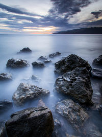Rocks in sea against sky during sunset