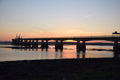 Silhouette bridge over river against sky during sunset