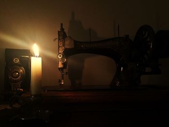 Illuminated candle on old sewing machine in dark room