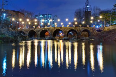 Illuminated bridge over river in city at night