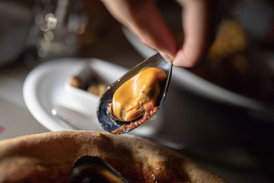 Woman holding mussel over plate at table