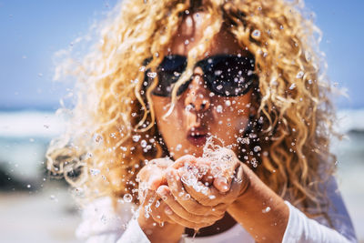 Close-up portrait of mature woman blowing water while standing at beach