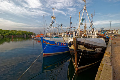 Boats moored at harbor against sky