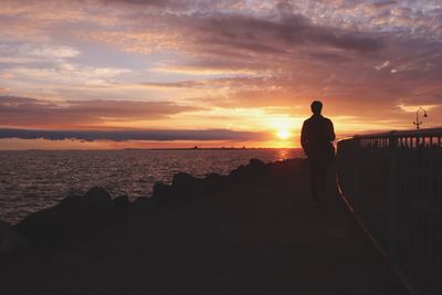 Silhouette man looking at sea against sky during sunset