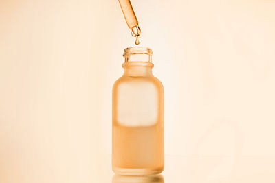 Face serum oil drop with dropper glass bottle pipette on yellow background close up