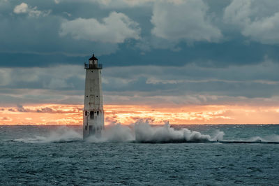 Lighthouse by sea against sky during sunset