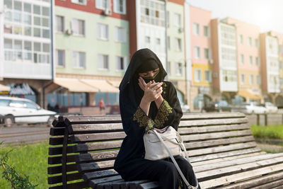 Muslim woman paints her eyes eyebrows while sitting on the street.