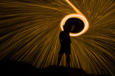 Full length of silhouette man standing against light trails