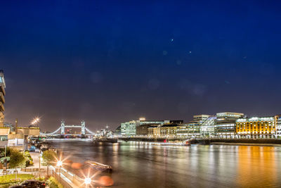 Illuminated city by river against sky at night