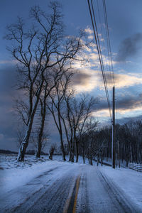 Road amidst bare trees against sky during winter