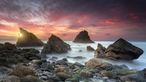 Rocks on shore against sky during sunset