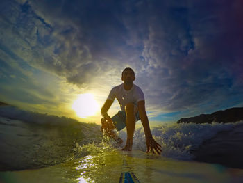 Man standing in sea against sky during sunset