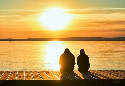 Rear view of silhouette people at sea during sunset