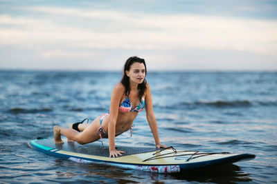 Young woman surfing in sea against sky during sunset