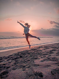 Man jumping on beach against sky during sunset