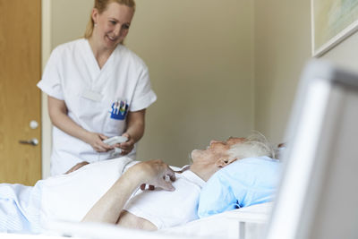 Smiling female nurse adjusting bed senior man's bed in hospital ward