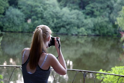 Rear view of woman photographing by lake