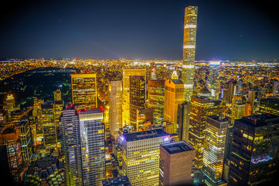 Illuminated modern buildings in city against sky at night