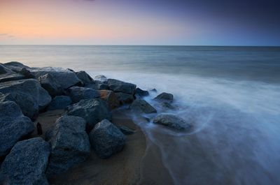 Scenic view of rocks at beach against sky during sunset