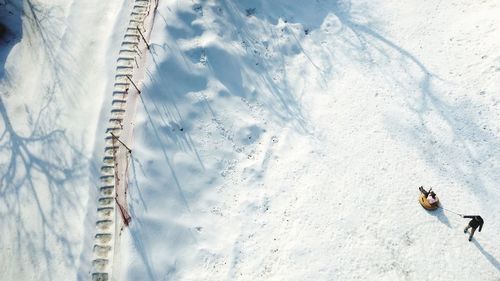 High angle view of man dragging woman on sledge during winter